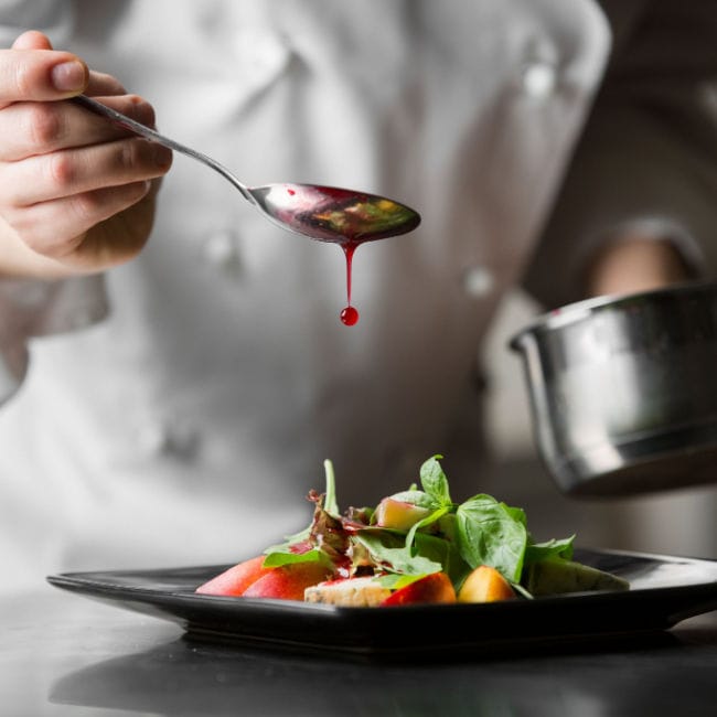 chef spooning sauce onto plated meal