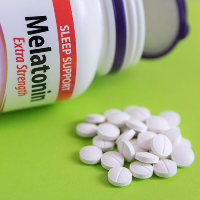 pile of melatonin supplements beside open melatonin bottle