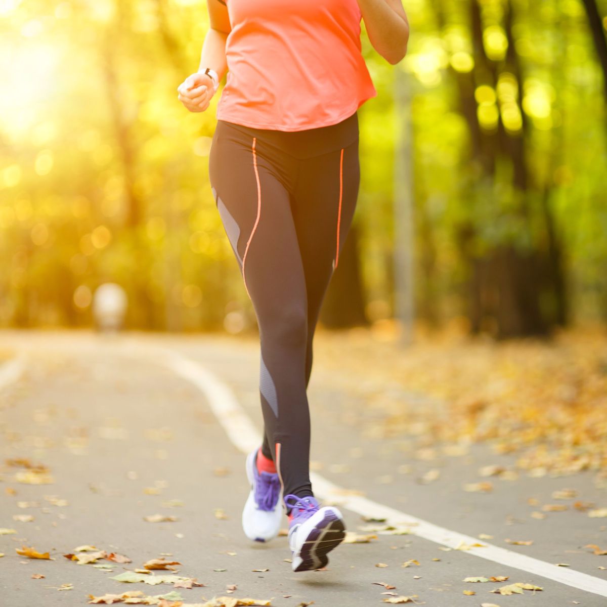 woman walking on road leaves black leggings pink long sleeved shirt sneakers