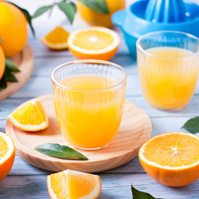 glass of orange juice besides sliced oranges