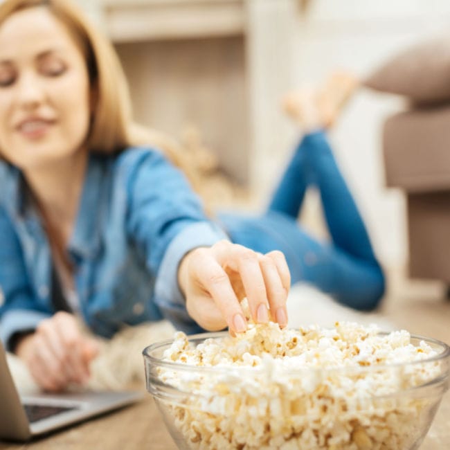 woman lying on stomach eating popcorn from bowl
