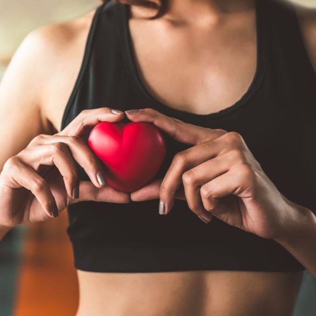 woman holding up red heart up to chest black sports bra top