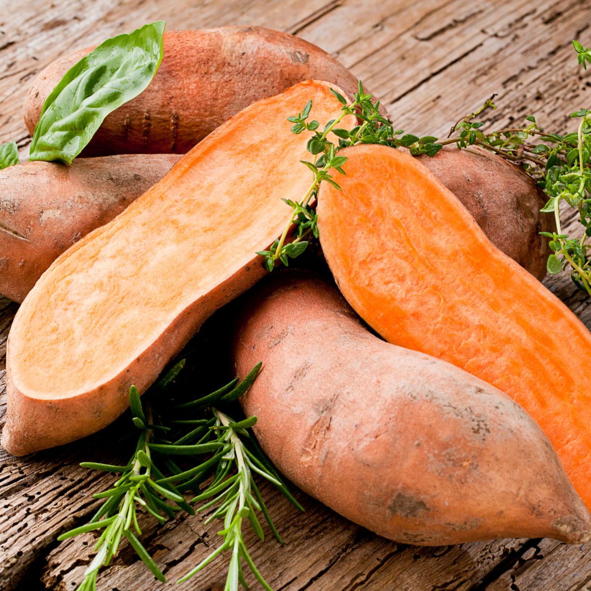 whole and halved sweet potatoes on wooden board