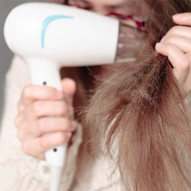 woman blow drying hair damage with white hair blow dryer