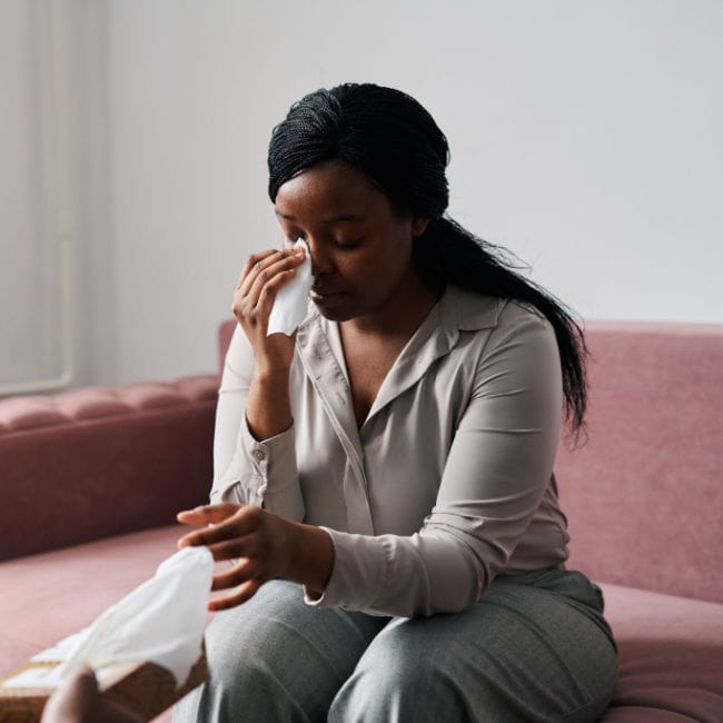 woman wiping tears with tissue on couch