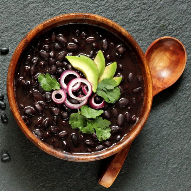 bowl of black beans topped with avocado, cilantro, and red onion