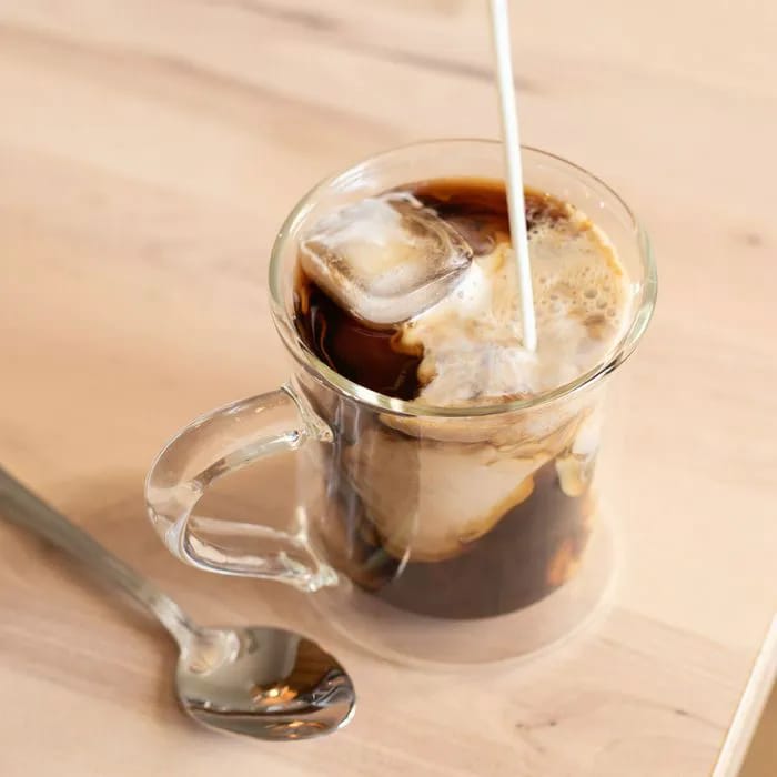 Pouring cream into an iced coffee mug.