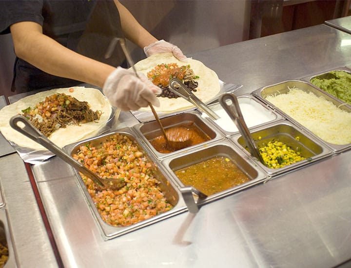 Chipotle worker making burrito at food station in Chipotle Mexican Grill