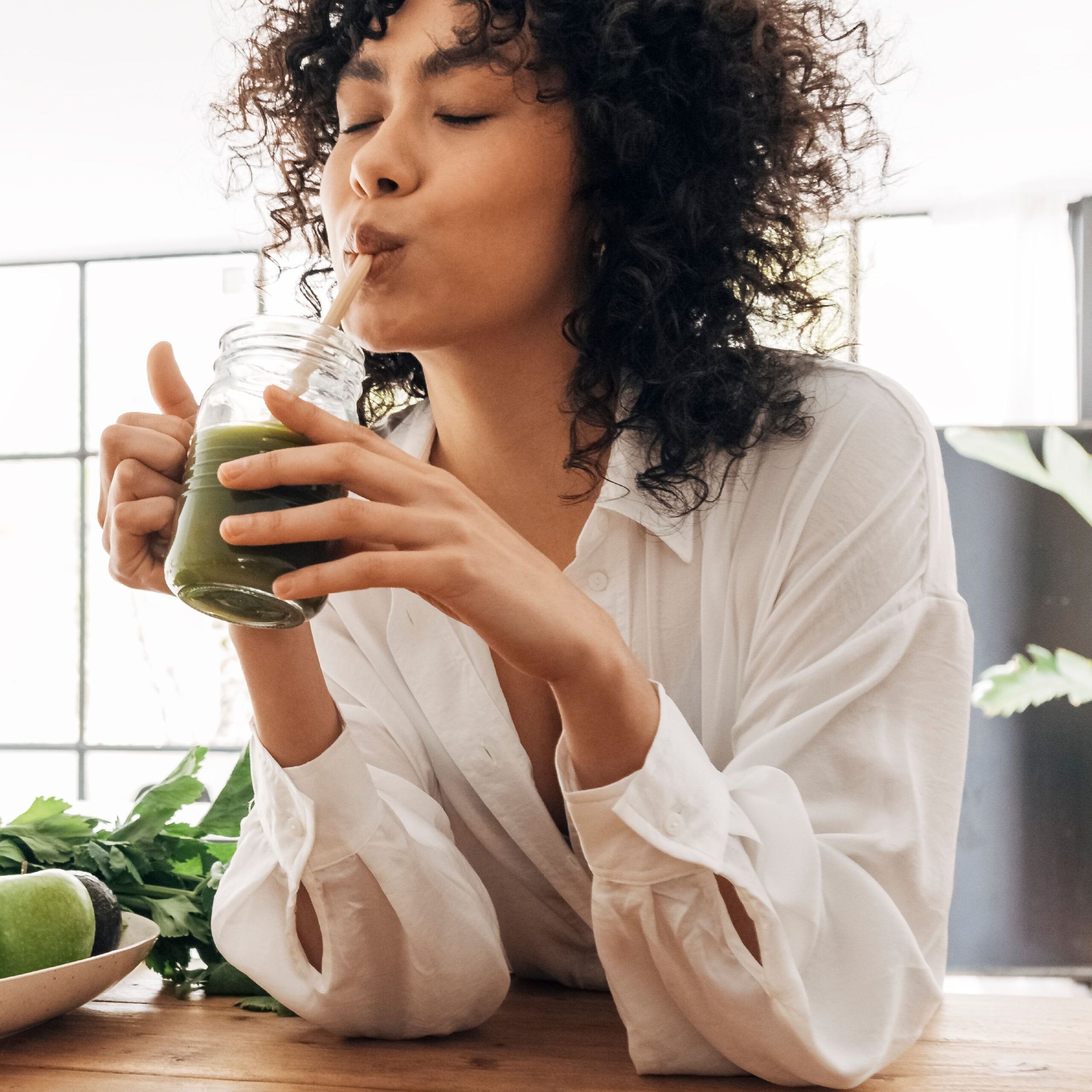 woman drinking green juice in kitchen