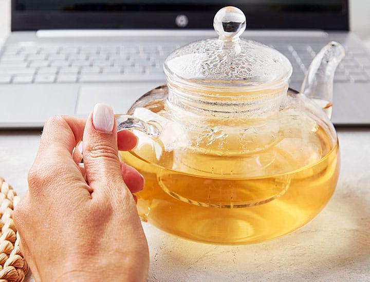 woman holding a glass teapot in front of laptop