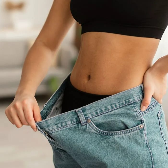 Woman with flat stomach trying on oversized jeans.