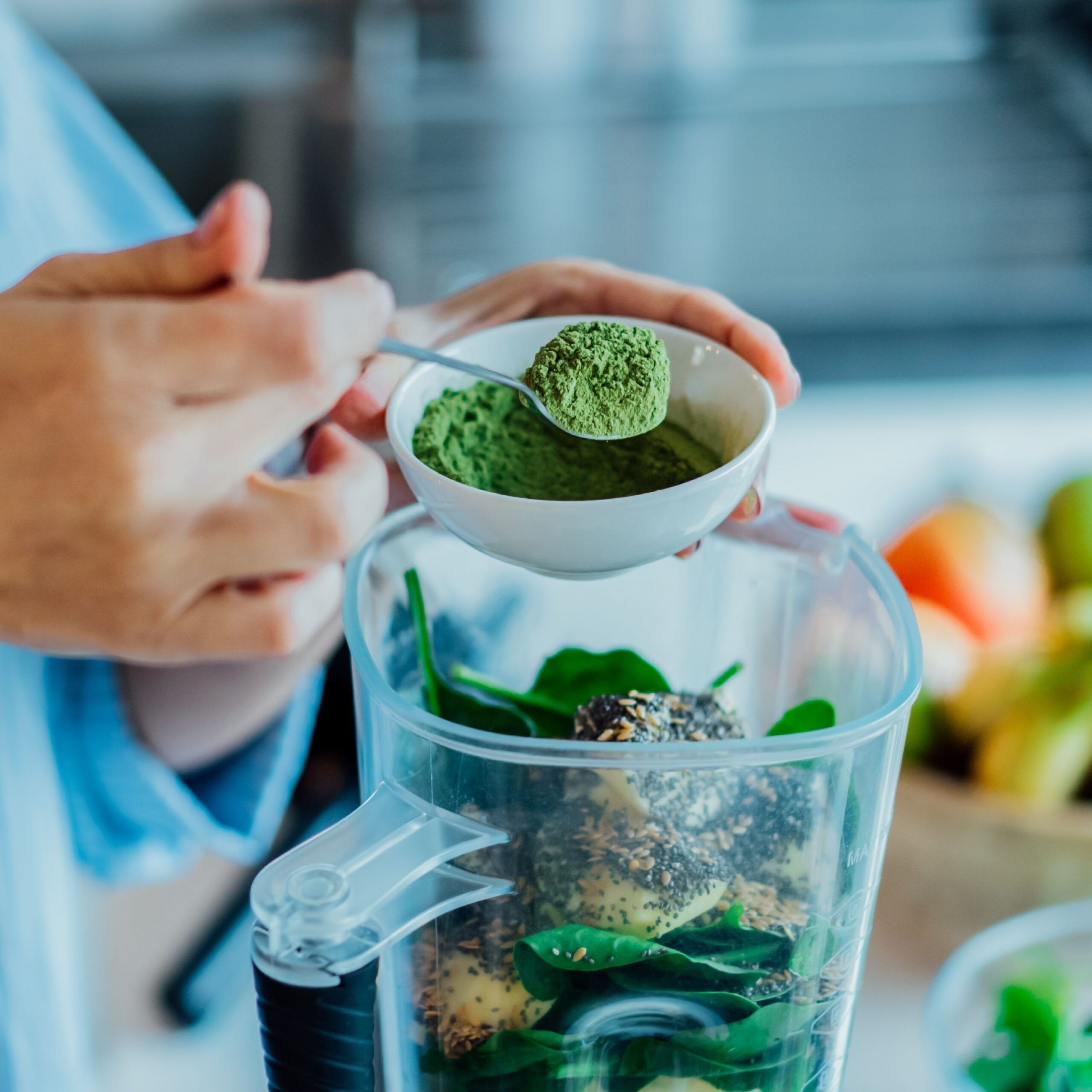 woman adding green powder to blender