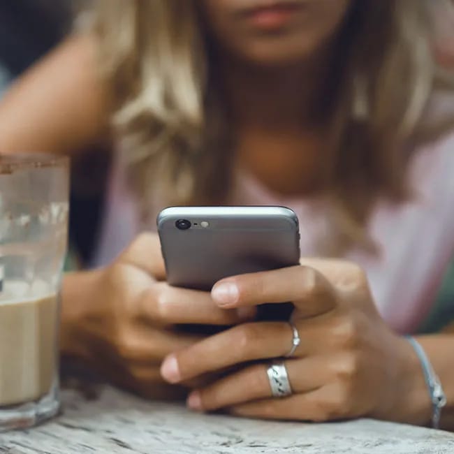 Girl using iPhone while enjoying coffee at a café.