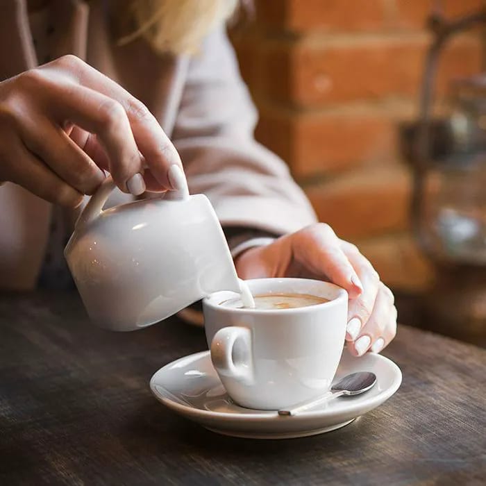 Woman pouring cream into coffee from a bottle