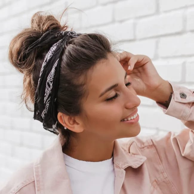 woman high bun brown hair curly high top knot white brick wall