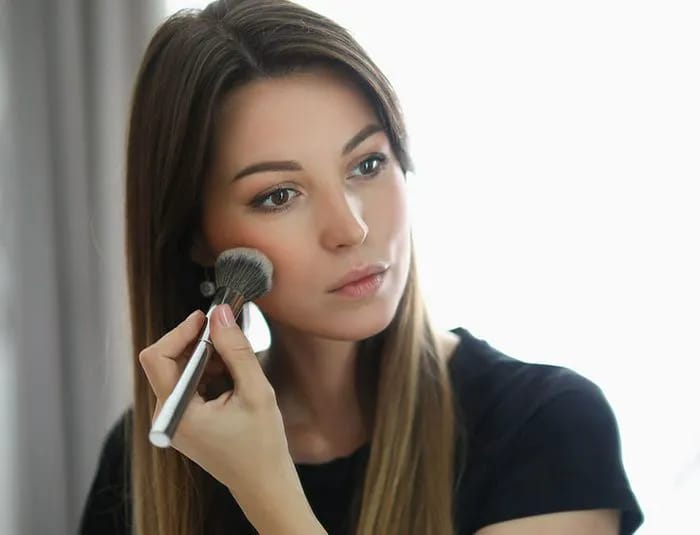 Woman applying blush with powder brush looking in mirror