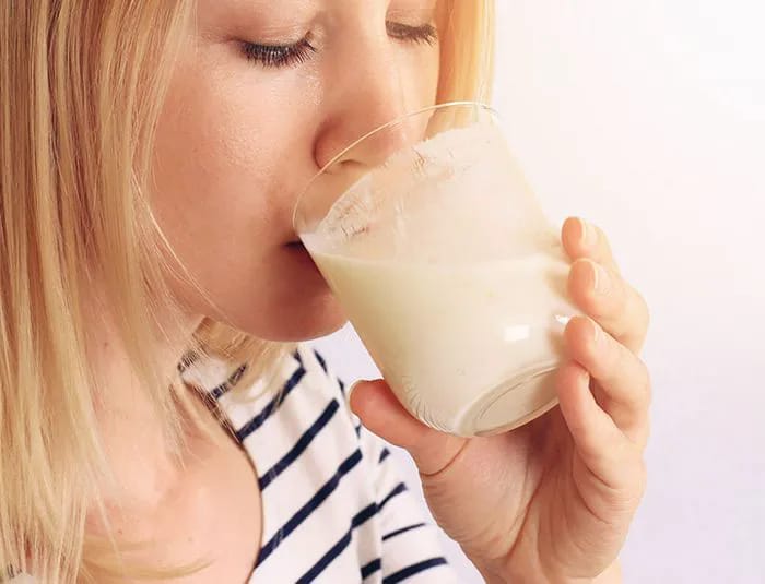 Blonde woman drinking a glass of oat milk