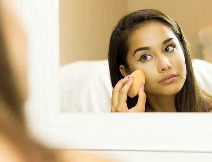 Woman applying foundation with beauty blender mirror