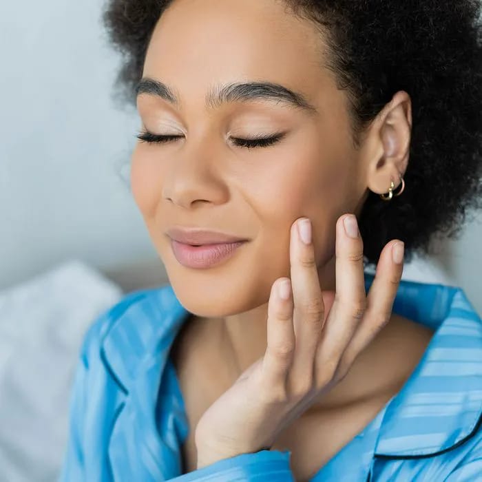 Young woman with healthy complexion touching her face.