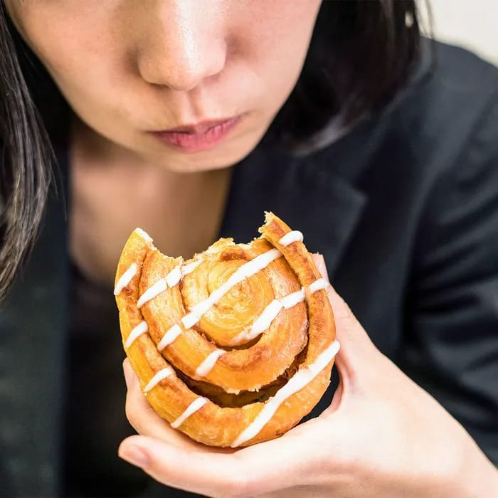 "Woman taking a bite out of a sweet pastry"
