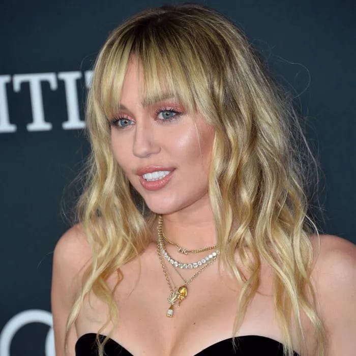 "Miley Cyrus headshot in a fringed gold mini dress"