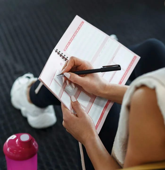 Woman journaling in a gym setting for fitness motivation.