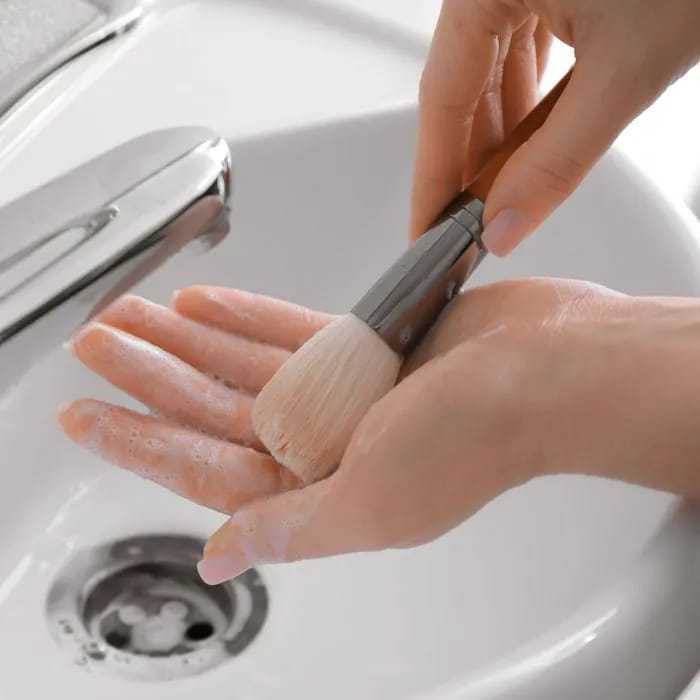 washing makeup brush under sink hand rubbing bristles with soap white sink silver faucet