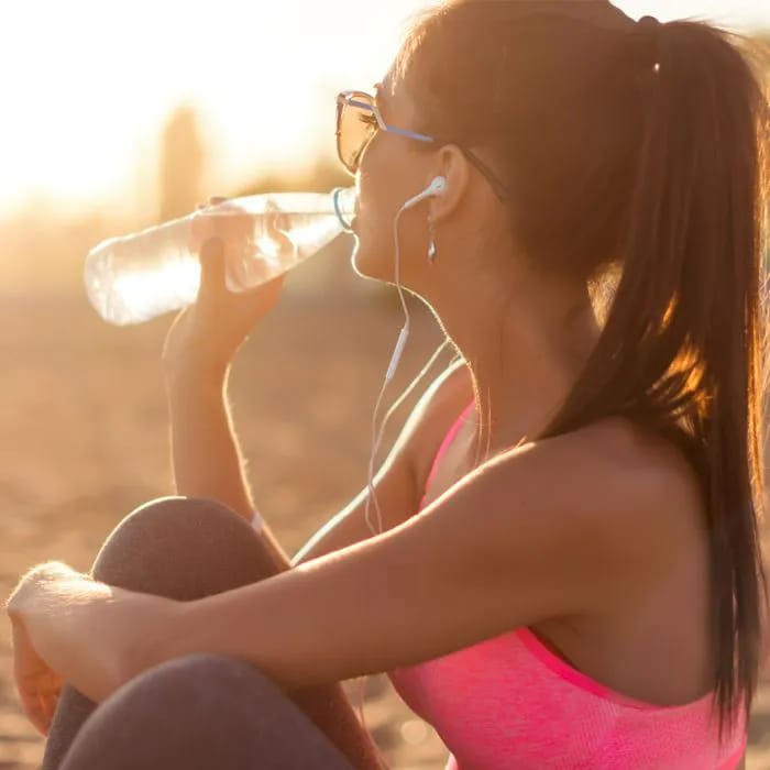 woman drinking water bottle plastic in the sunlight hair ponytail pink tank top glasses earbuds