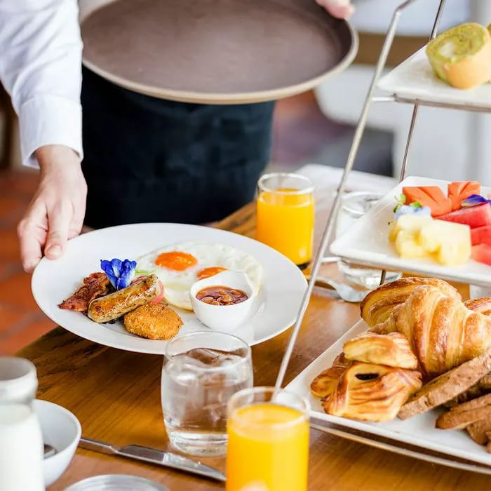 Waiter serving hotel breakfast with eggs and pastries.