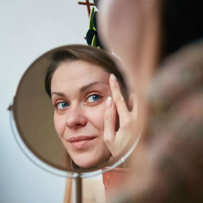 Aging woman examining her skin in a mirror.