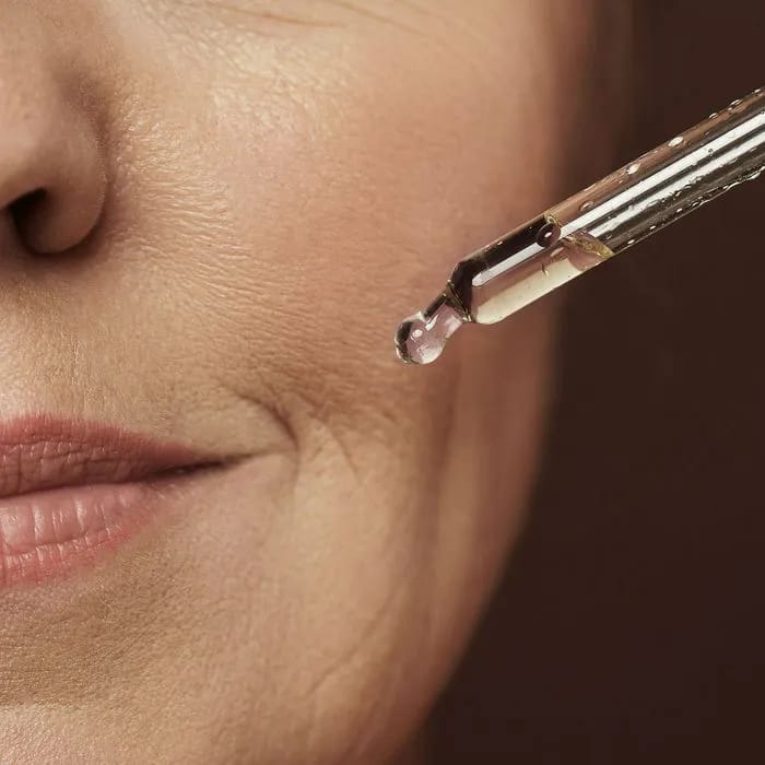Woman using serum dropper near her lips.