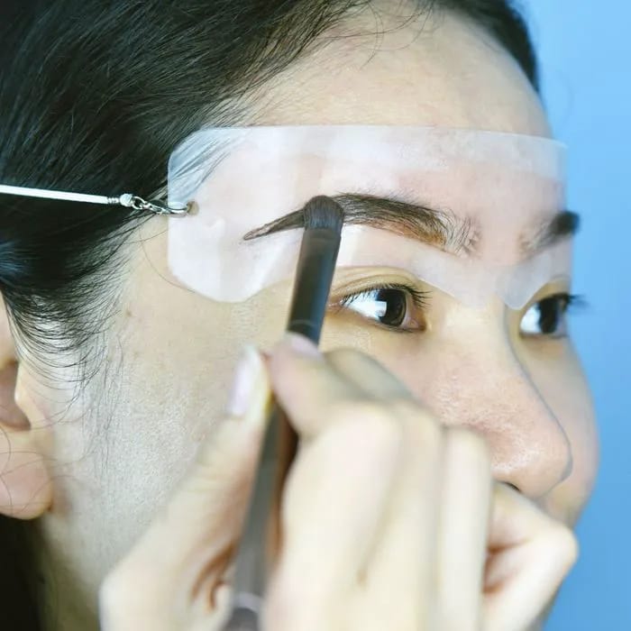 "Woman using eyebrow stencil to fill in brows"