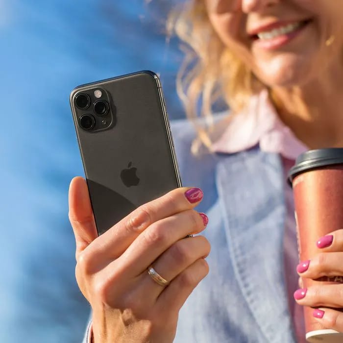 Woman smiling while using a black iPhone outdoors