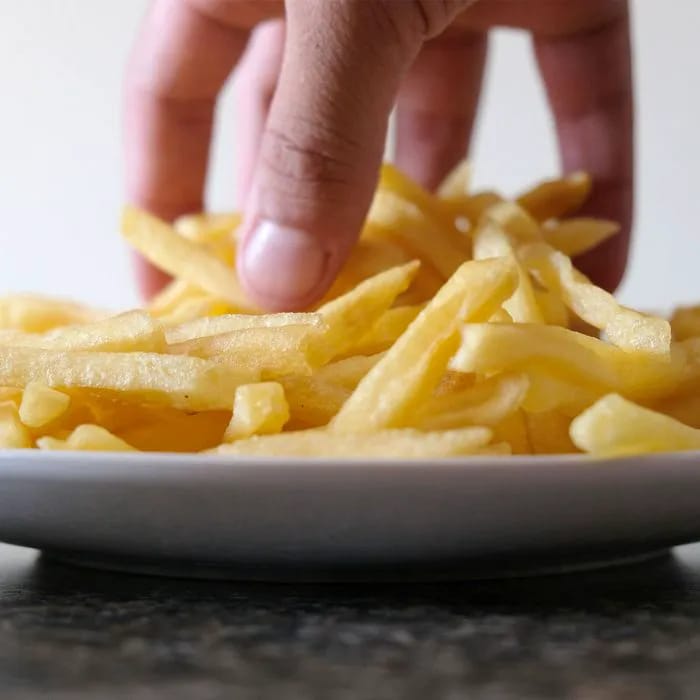 Hand reaching for unhealthy French fries on a plate.