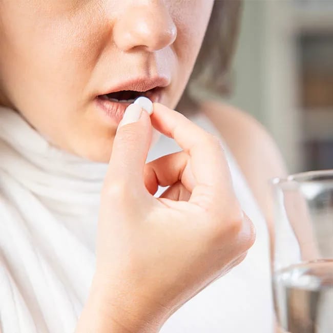 Woman taking a supplement with a glass of water.