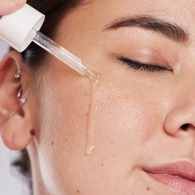Woman applying skincare oil to her cheek