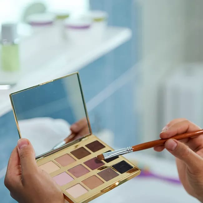 Woman applying makeup using an eyeshadow palette.