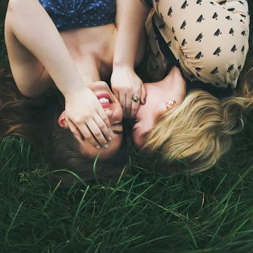 Group of girls playing and laughing in a grassy field.