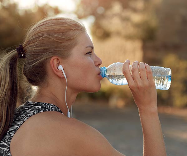 woman listening to music and drinking out of water bottle