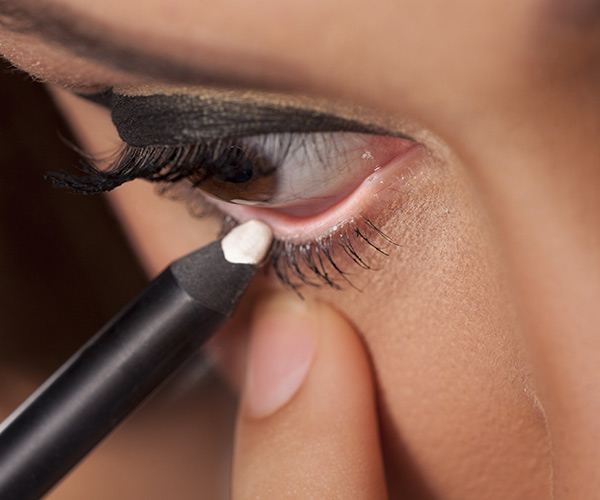 woman applying white eyeliner to bottom waterline