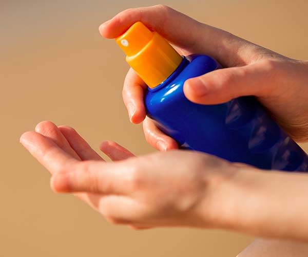 woman spraying sunscreen to hand
