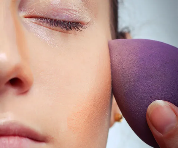 woman applying foundation with purple beautyblender