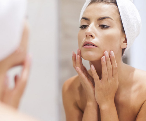 woman applying skincare product in mirror