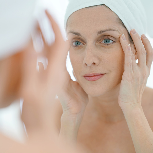 woman using skincare products in mirror