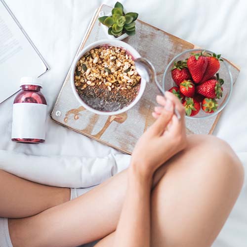 woman eating breakfast of yogurt cereal and strawberries in bed