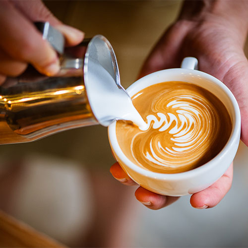 A person pouring froth on a latte.