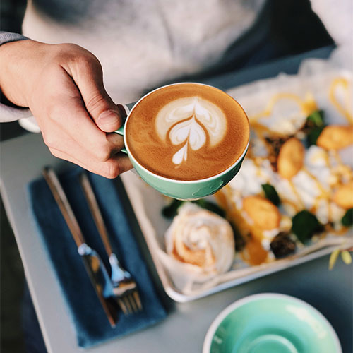 A person holding a latte with breakfast.