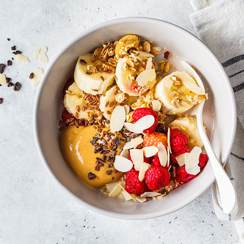 A bowl of oatmeal with fruit and peanut butter.