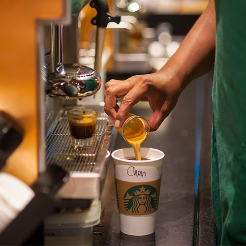 A person pouring expresso into a Starbucks cup.
