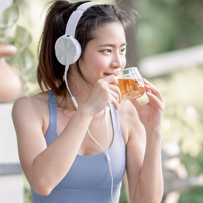 woman in athletic clothes drinking tea outside with headphones on